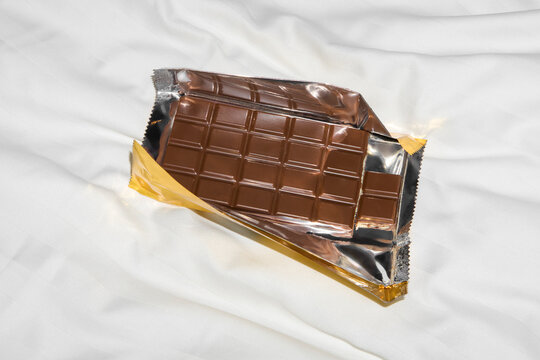 Milk Chocolate Bar in Luxurious Gold Wrapper on Soft White Bed Fabric