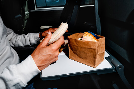 inside a dark train carriage, a man eats a banana beside a sandwich