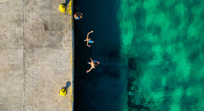 Aerial view of kids jumping into emerald water from pier
