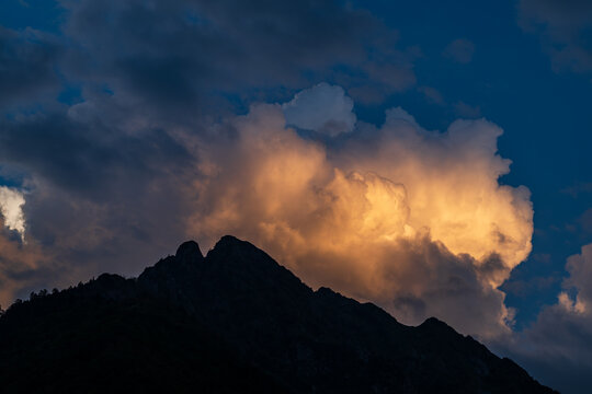 Dramatic sky with clouds and silhouette of a mountain peak at sunset in summer
