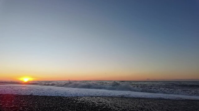 Golden sunset glows as waves crash onto pebble shore along batumi black sea coastline.