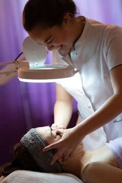 Professional beautician performing facial massage in modern beauty salon