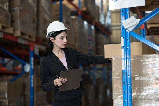 Female warehouse worker checking incoming items on shelf pallet at storage warehouse