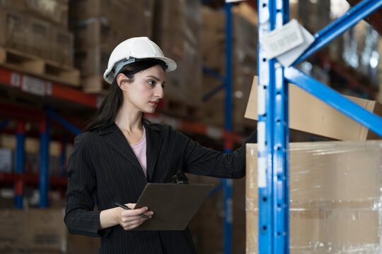 Female warehouse worker checking incoming items on shelf pallet at storage warehouse