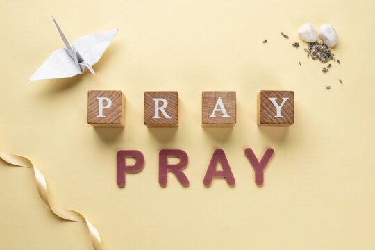 Spiritual Composition with the Word Pray Wooden Blocks Origami Crane and Decorative Elements on a Yellow Background