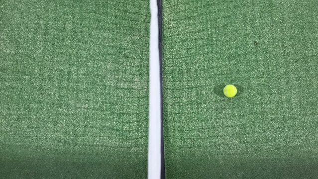 Top-down aerial view of a padel ball on the right side of the net, with a symmetrical centered composition dividing the court into left and right halves for sports and competition concepts.
