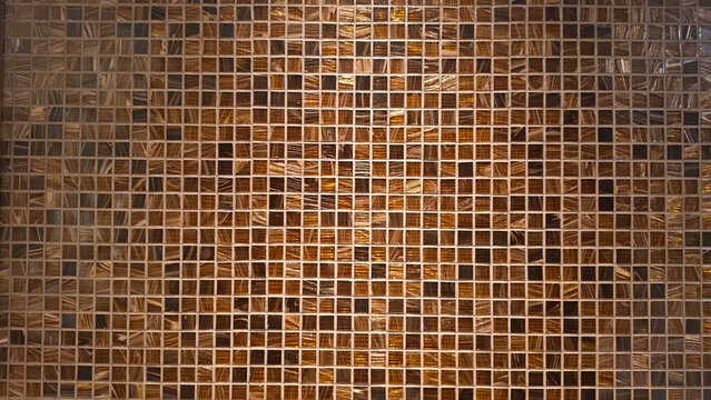 Close-up of small square brown and dark brown mosaic tiles arranged in a gradient pattern on an interior wall, creating an abstract geometric texture and modern decorative background.