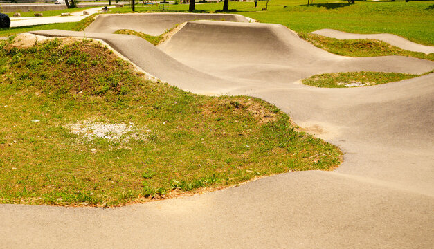 Side view of an empty asphalt pump track with humps and curves in a green public park. Ideal for cycling, skateboarding, outdoor sports, and active lifestyle concepts.
