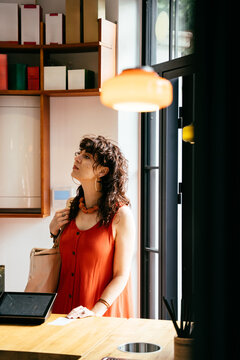 Curious middle-aged woman in orange dress at specialty cafe counter, vertical shot
