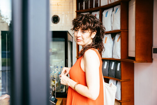 Thoughtful middle-aged woman in orange dress choosing coffee at modern specialty cafe