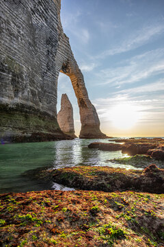 Sunlit sea arch and chalk cliffs at Etretat, Normandy, France, with rocky tide pools in the foreground
