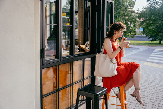 Relaxed middle-aged woman drinking iced matcha outside modern specialty coffee shop