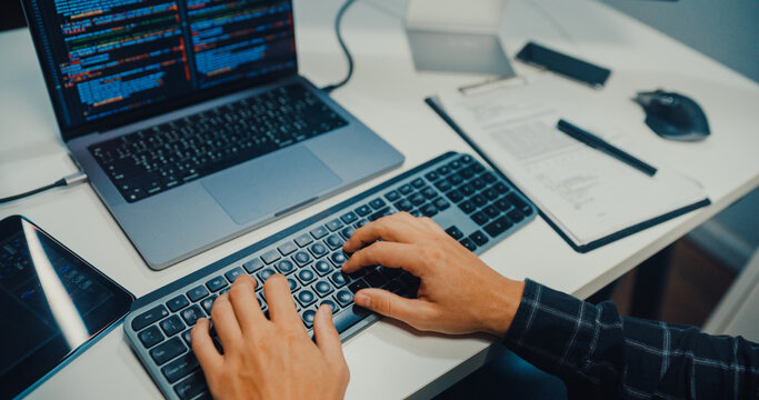 Close up young Caucasian male programmer writes code using multiple screens in home office workspace. AI development, cybersecurity, network database system, software engineering, remote tech startup.
