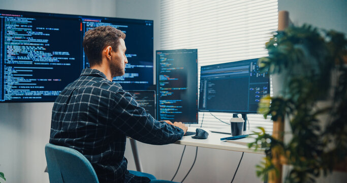 Young Caucasian male programmer writes code using multiple screens in home office workspace. AI development, cybersecurity, network database system, software engineering, remote tech startup concept.