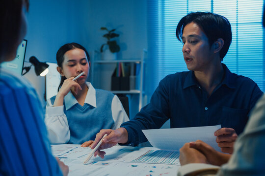 Asia businesspeople presentation sales meeting plan statistics brainstorm and work with paperwork around table in office conference room at night. Business finance partner strategy investment success.