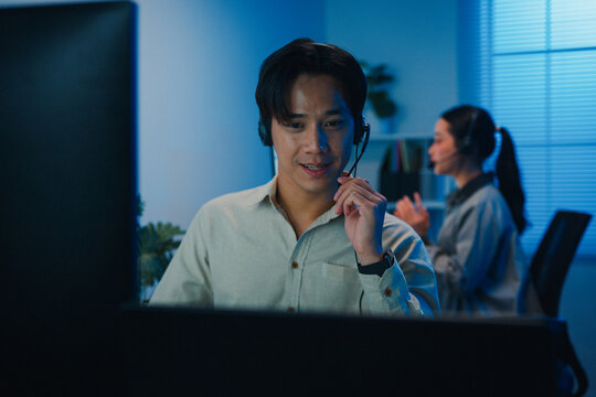 Gen z Asia young call center team or customer support service executive use computer and microphone headset work technical e commerce support in late night office. Telemarketing or sales job concept.