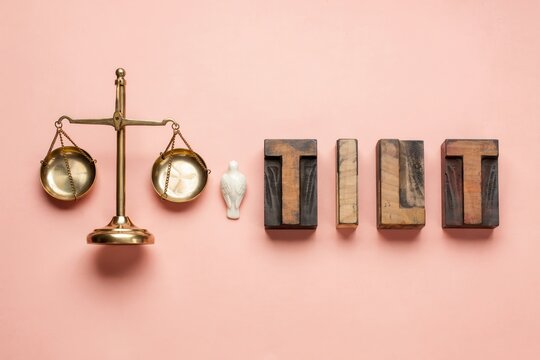 Scale of justice next to wooden letters spelling tilt concept of legal bias imbalance and tipping the scales of law
