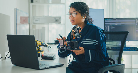 Young African American female robotics engineer discussing mechanical part on video call in laboratory. Remote work, virtual training, online meeting, future technology, technical support concept.