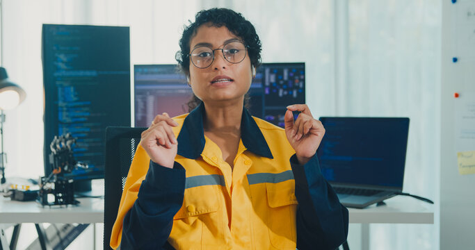 Young African American female robotics engineer discussing mechanical part on video call and looking at camera in laboratory. Remote work, virtual training, online meeting, future technology concept.
