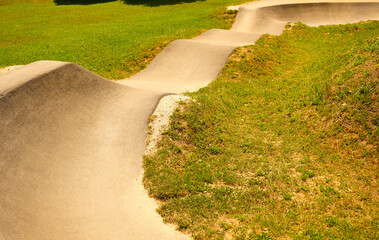 High angle view of a wavy asphalt pump track section in a green public park on a sunny day. Great for modern sports, active lifestyle, cycling, and urban design themes. © YuliiaKettu