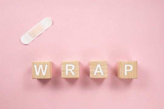 Word Wrap spelled with wooden toy blocks next to a plaster bandage on pink background