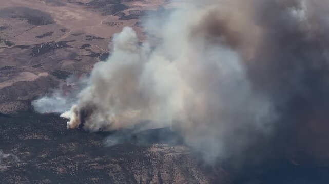 flying along a huge forest fire in a wooded mountain region, with massive smoke rising into the atmosphere - 4k aerial video footage 