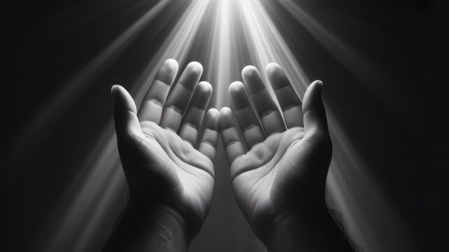 Close up of hands held in prayer under dramatic divine light rays in black and white