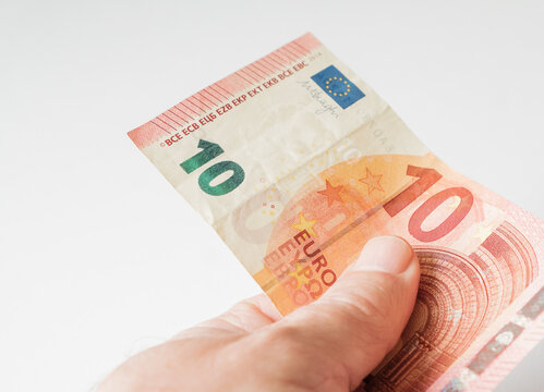 A hand holding a single ten Euro banknote over a plain white background