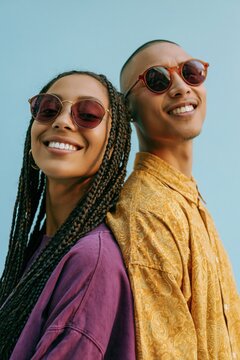 Smiling young couple back to back wearing round sunglasses and colorful shirts for lifestyle portrait background and casual fashion banner
