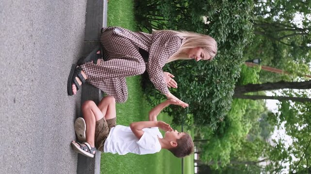 Vertical video. Joyful interaction. Childhood fun. Happy mother cheerful son playing in green park enjoying hand clap game summer family leisure outdoor.