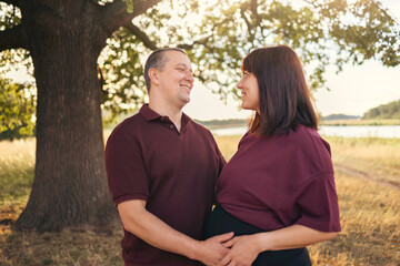 Fototapeta premium Pregnant woman and her partner walking together at sunset, holding hands