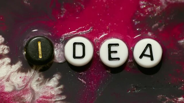Idea text. Glitter ink. Defocused red white purple colorful black shimmer letters texture on abstract creative marble art background.