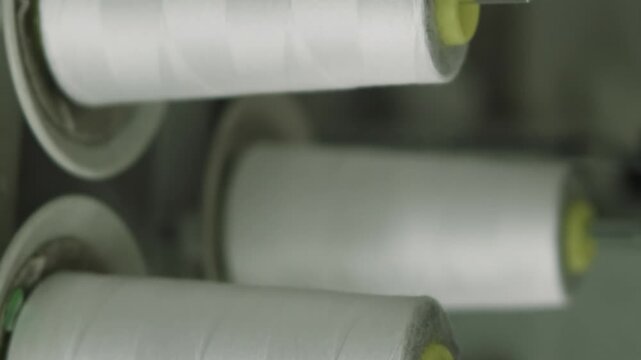 Vertical video. Thread spool factory. Textile studio equipment. Bobbins with white string in professional tailoring workplace. Materials for clothing industry.
