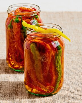 Two glass jars packed with pickled chili peppers in brine on a linen surface, featuring vibrant orange and yellow colors for food preservation and gourmet cooking concepts