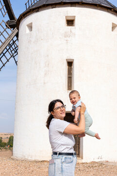 Mother holding baby laughing outdoors by a historic windmill