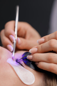 Closeup of female receiving led eyelash extension treatment with tweezers and eye pads