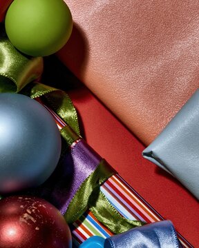 Colorful festive gifts and satin ribbons with matte baubles on a bold red surface for a vibrant Christmas and New Year greeting background