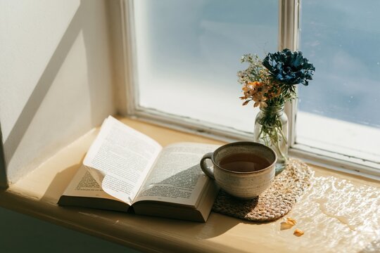 An open book and a cup of tea on a golden windowsill during a cozy morning for slow living and reading ritual themes