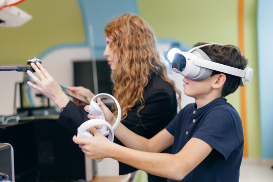 Boy testing virtual reality headset with instructor in classroom, Concept innovative education