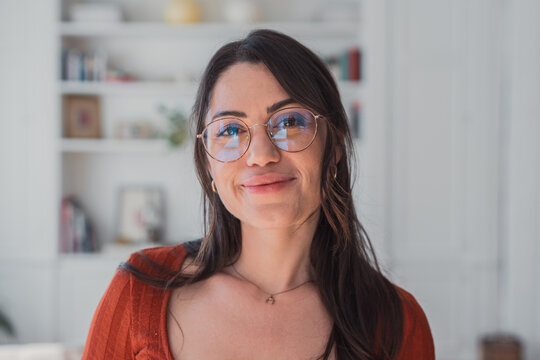 Woman with dark hair and gold-rimmed eyeglasses smiling softly, reflecting a confident and intelligent persona in an indoor setting, representing business, learning, and everyday life