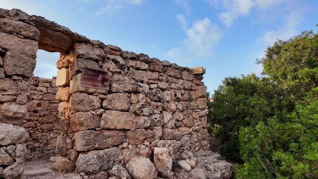 Stone wall frames weathered plaque. Historical text etched into aged surface. Sunlight glints off crumbling stones. Plaque recounts rural farming traditions