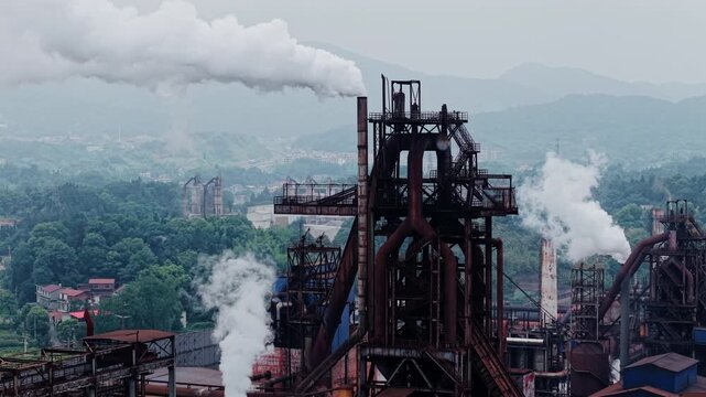 Static wide angle shot of heavy industrial factory emitting dense white smoke and steam under overcast sky. Ideal for environmental pollution, industrial production, and energy impact concepts.
