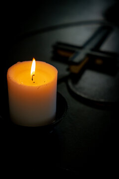 Burning candle with blurred Christian cross in a dark church interior