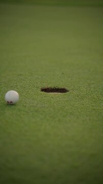 Person playing mini golf hitting the ball into the hole with a putter on an artificial grass course