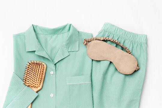 Flat lay with green Pajama, beige sleep eye mask, hair brush on white sheet. Top view trend mint colored woman home sleepwear and accessories on bedclothes. Cozy pyjamas of shirt and shorts for sleep
