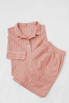 Top view of pink striped pajama suit on white bed. Minimal style, cozy, comfort pyjamas. Sleepwear fashion concepts, wellness, calm lifestyle, home aesthetics, closeup fabric texture, feminine design