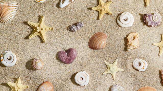 Natural heart stone among yellow starfish and seashells on sand, beach find as symbol love and lucky. Sunlit minimal summer aesthetic photography. Top view romance summer pattern, beige pastel color.