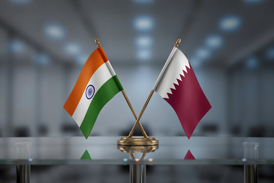 Small national flags of india and qatar on a glass desk in a blurred office, representing diplomatic cooperation and international relations