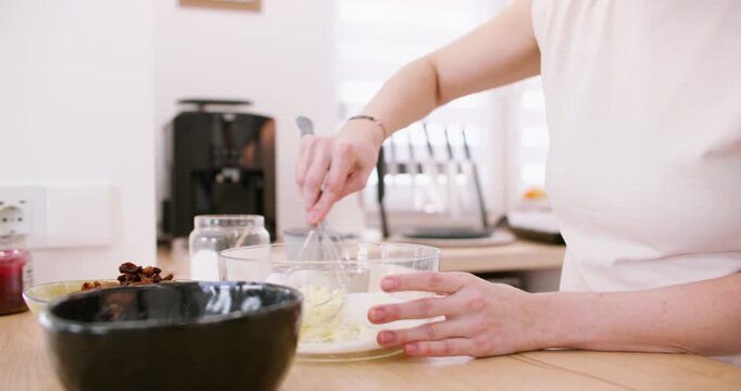 Bakery work. Mixing process. Female chef hand whisking butter sugar ingredients for homemade dough in glass bowl on modern countertop.