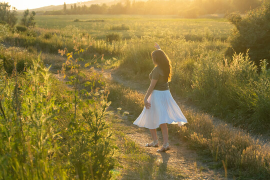 Young woman walking on a meadow path during golden hour sunset